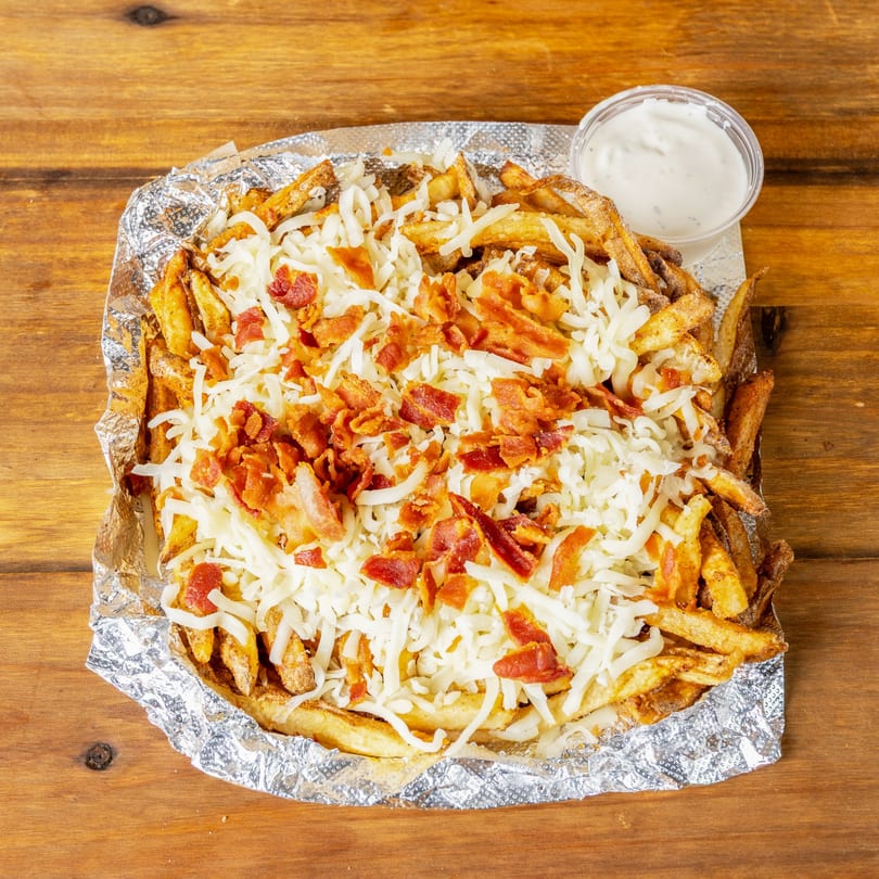 Fries topped with shredded white cheese and crispy bacon bits, served with a side of ranch.