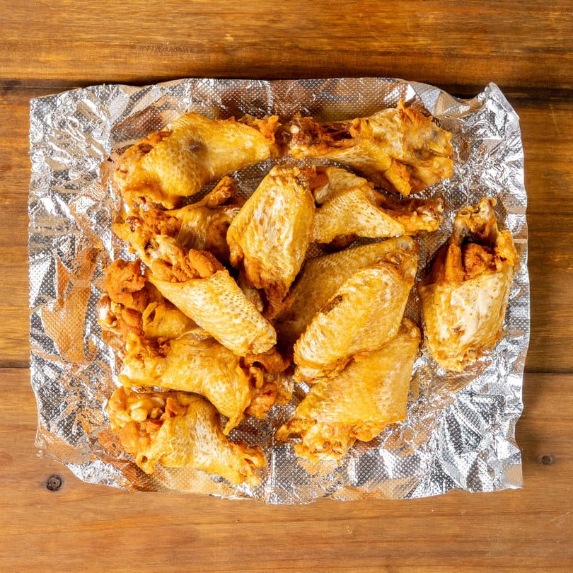 Golden-brown fried chicken wings and crispy pieces on aluminum foil, centered on a wooden table.