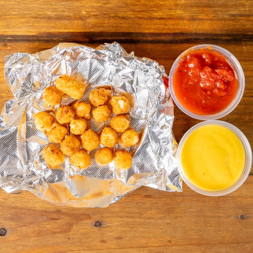 Golden tater tots on foil with cups of salsa and cheese sauce on a wooden table.