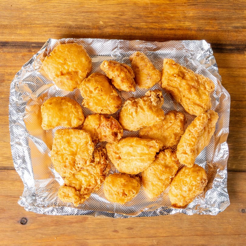 Golden-brown fried chicken nuggets and tenders on crinkled aluminum foil, on a wooden table.